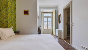 A hotel room with a large bed, a chair, a radiator, and a door leading to a balcony.