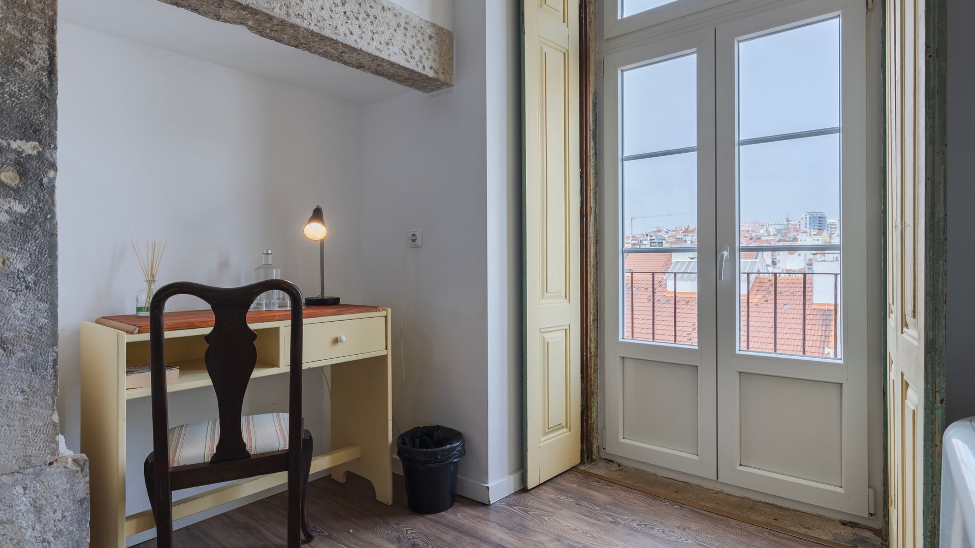 A room with a desk, chair, and a window with a view of buildings.