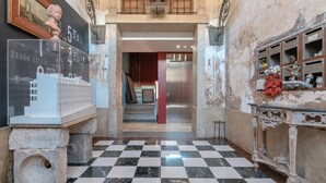 A lobby with a checkered floor, a staircase, a modern elevator, and a decorative cabinet with small figurines.