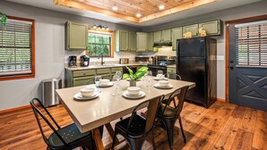 A modern kitchen with green cabinets, a black refrigerator, and a dining table set for six. - Modern 4-bedroom Cabin w/ Hot Tub/Game Room/Fire Pit/Backyard (Sevierville)