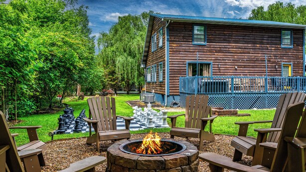 A wooden cabin with a fire pit and Adirondack chairs in the yard. - Modern 4-bedroom Cabin w/ Hot Tub/Game Room/Fire Pit/Backyard (Sevierville)