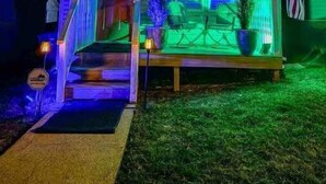 Uma casa com um letreiro de neon que diz "Glow Hill" e um alpendre com área de estar ao ar livre.