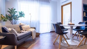 A modern living room with a sofa, dining table, chairs, and a large window with curtains. - Emilia Elegant and Modern Two Steps from Rome (ROMA)