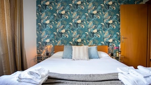 A hotel room with a bed, a nightstand, a wooden wardrobe, and a floral wallpaper. - Emilia Elegant and Modern Two Steps from Rome (ROMA)