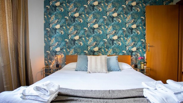 A hotel room with a bed, a nightstand, a wooden wardrobe, and a floral wallpaper. - Emilia Elegant and Modern Two Steps from Rome (ROMA)