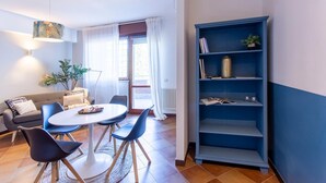 A modern living room with a round table, blue chairs, a grey sofa, and a blue bookshelf. - Emilia Elegant and Modern Two Steps from Rome (ROMA)