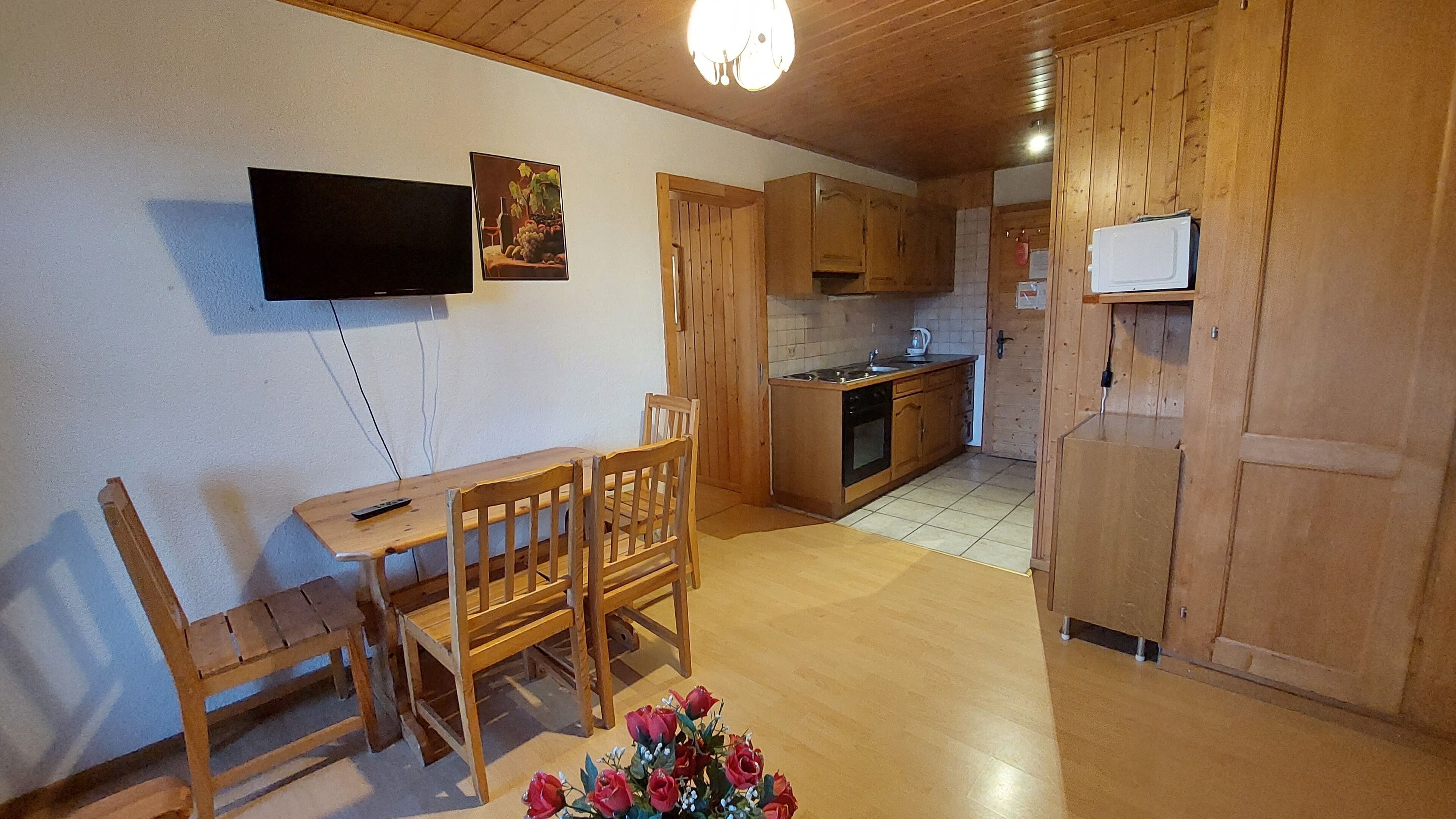 A wooden interior with a dining table and chairs, a kitchen area with wooden cabinets, and a flat-screen TV mounted on the wall.