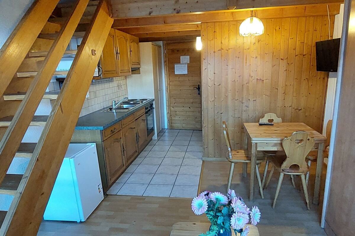 A rustic wooden interior with a kitchen, dining area, and staircase.
