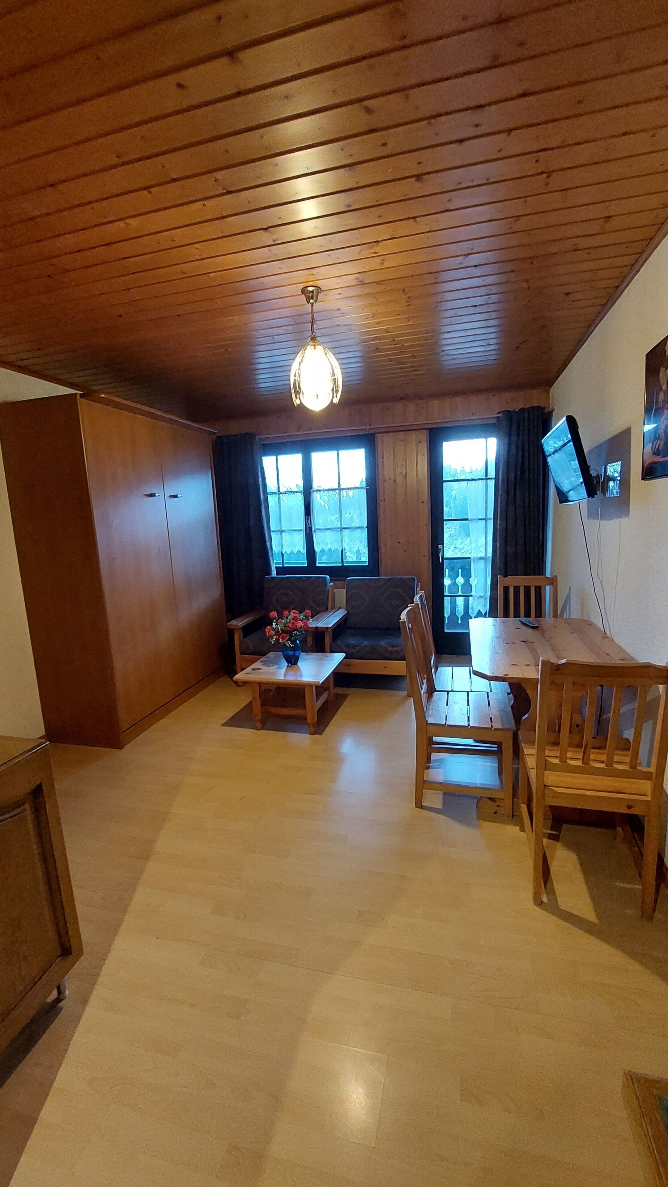 A cozy living room with wooden furniture, a sofa, a coffee table, and a TV mounted on the wall.