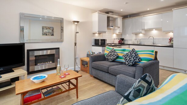 A modern living room with a fireplace, a sofa, a coffee table, and a television. - Park Place Court 2 - Close to Beach, Parking (Tenby)
