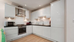 A modern kitchen with white cabinets, a microwave, stove, oven, and a sink. - Park Place Court 2 - Close to Beach, Parking (Tenby)