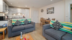 A modern apartment with two grey sofas, a wooden dining table, and a kitchen with white cabinets. - Park Place Court 2 - Close to Beach, Parking (Tenby)