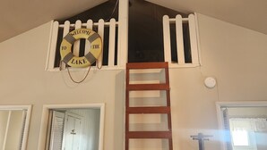 A loft bedroom with a wooden ladder leading to a lofted sleeping area, a ceiling fan, and a welcome sign to the lake. - Cozy Cottage with water access, Newly remodeled  (Celina)