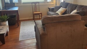 A living room with a brown sofa, a wooden chair, a small table with a plant, and a TV on a stand. - Cozy Cottage with water access, Newly remodeled  (Celina)