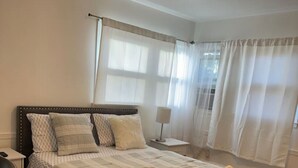 A neatly arranged bedroom with a bed, bedside tables, and a window with curtains. - Comfortable unique space (Colonie)