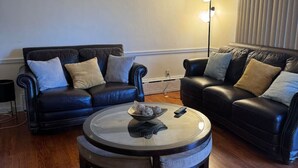 A living room with two black leather sofas, a glass coffee table, and a floor lamp. - Comfortable unique space (Colonie)