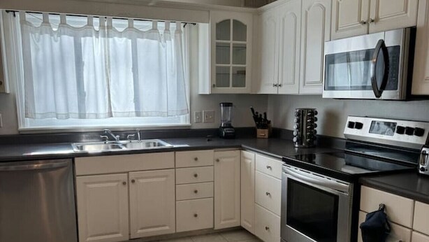 A kitchen with white cabinets, a stainless steel refrigerator, a microwave, an oven, and a sink. - Comfortable unique space (Colonie)