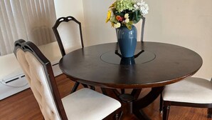 A round dining table with a blue vase of flowers, surrounded by four upholstered chairs with wooden frames. - Comfortable unique space (Colonie)