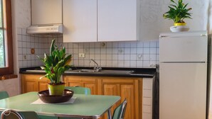 Una cocina con armarios de madera, un lavamanos, una estufa y un refrigerador. Hay una mesa con sillas y una planta en maceta sobre ella.