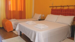 Habitación de hotel con dos camas individuales, una cama grande, una mesita de noche con lámpara y una ventana con cortinas.
