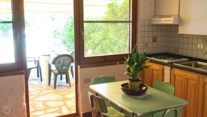 Una cocina con suelo de piedra, una mesa de comedor con sillas, una planta en maceta y vistas al exterior.