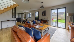 A spacious living area with a wooden staircase, leather sofas, a wooden coffee table, and a sliding glass door leading to a patio. - Nouelig - A 150m de la plage de la Ria (Plouhinec)
