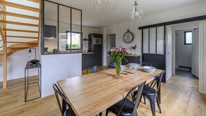 A modern kitchen with a wooden staircase, a dining area with a wooden table and chairs, and a large mirror on the wall. - Nouelig - A 150m de la plage de la Ria (Plouhinec)