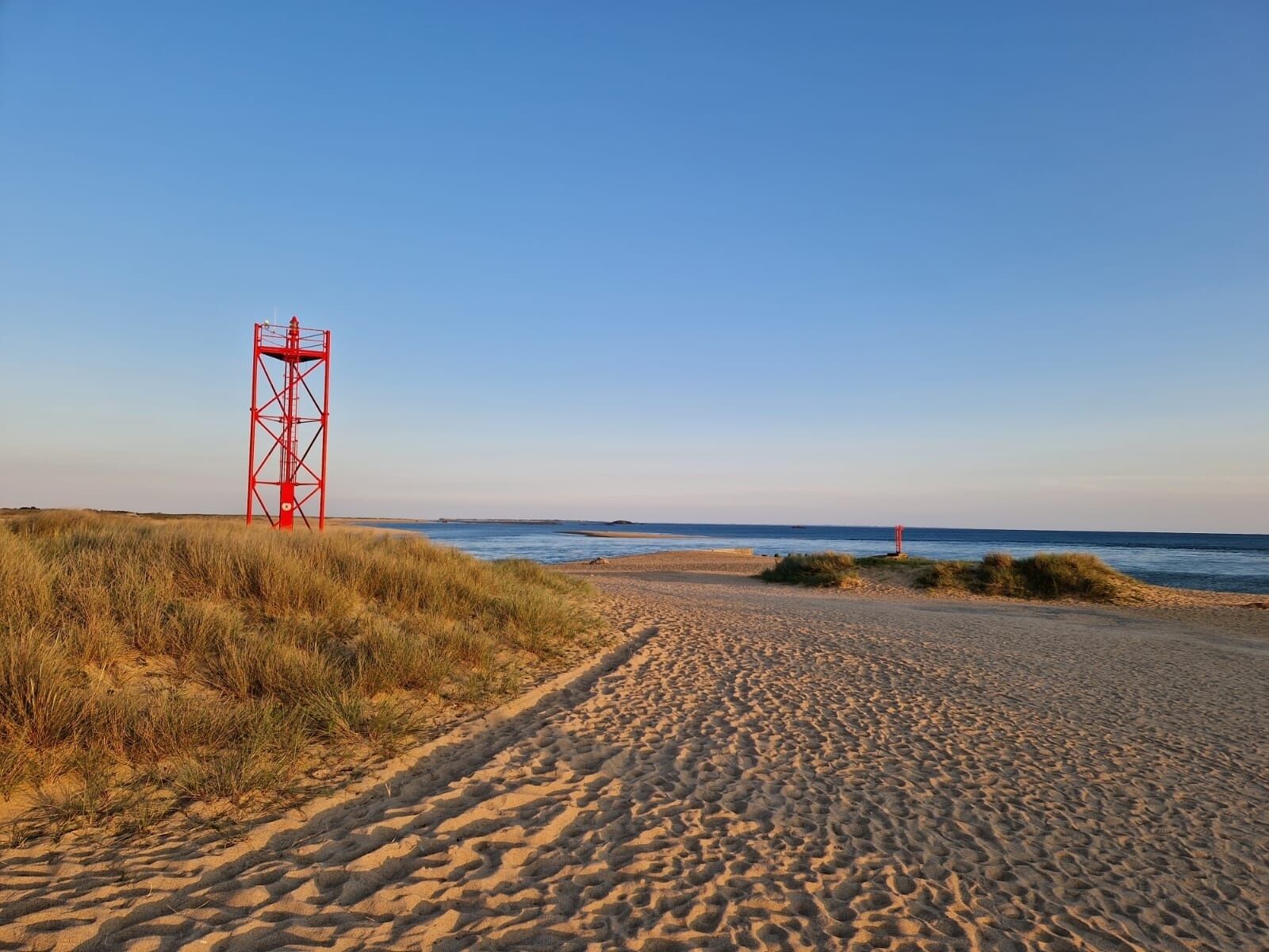 A sandy beach with a red metal structure in the distance.