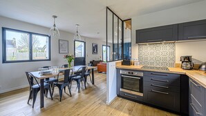 A modern kitchen with a wooden dining table, black chairs, and a built-in oven. - Nouelig - A 150m de la plage de la Ria (Plouhinec)