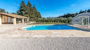A swimming pool with a stone deck, a covered outdoor seating area, and a greenhouse structure. - Gîte du Mas Saint Paul - Maison avec piscine (Travaillan)