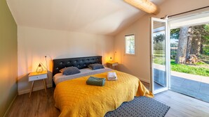 A bedroom with a large bed, wooden headboard, bedside lamps, and a view of a garden through a sliding glass door. - Gîte du Mas Saint Paul - Maison avec piscine (Travaillan)