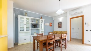 A dining area with a wooden table and chairs, a white cabinet with glass doors, and a ceiling light. - Villa by the sea with garden (Piana Calzata)