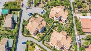 An aerial view of a residential area with multiple houses, a parking lot, and a green space with palm trees. - Villa by the sea with garden (Piana Calzata)