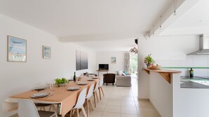 Un espace repas moderne comprenant une longue table, des chaises et un coin cuisine avec un comptoir et des appareils électroménagers.