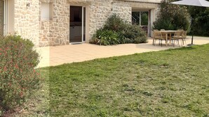 Une maison en pierre dotée d’une grande fenêtre, d’un balcon et d’une terrasse aménagée avec du mobilier d’extérieur.