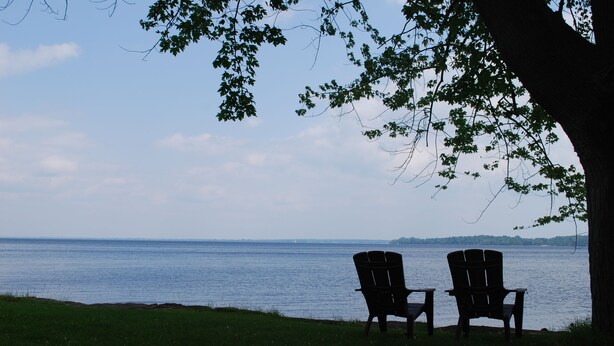 Two Adirondack chairs facing a body of water with a distant shoreline and trees in the background.