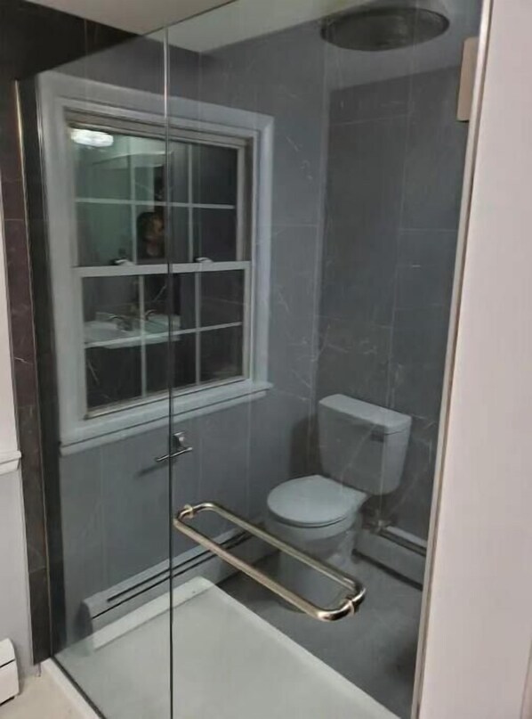 A small, enclosed shower area with a glass door, a toilet, and a window.