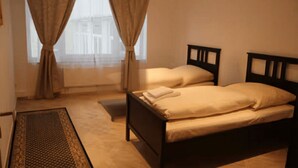 A bedroom with two beds, a window with curtains, a small rug, and a wooden headboard. - Washington Apartment (Hannover)