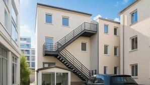 A multi-story building with a central staircase, a car parked in front, and a clear sky. - Washington Apartment (Hannover)