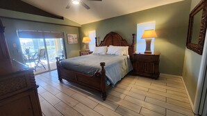 A bedroom with a wooden bed, two bedside tables with lamps, a ceiling fan, and a sliding glass door leading to an outdoor area.