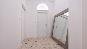 Un couloir étroit aux murs blancs, doté d’un sol carrelé et d’une porte blanche au fond.