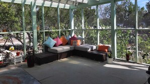 Una habitación soleada con un ventanal grande, una zona de estar con cojines y una mesita.