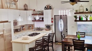 Una cocina con una isla central, armarios blancos y un comedor con sillas de madera.