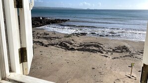 Blick auf einen Strand durch ein Fenster, mit felsiger Küste und Wellen.