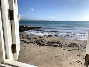 Blick auf einen Strand durch ein Fenster, mit felsiger Küste und Wellen.
