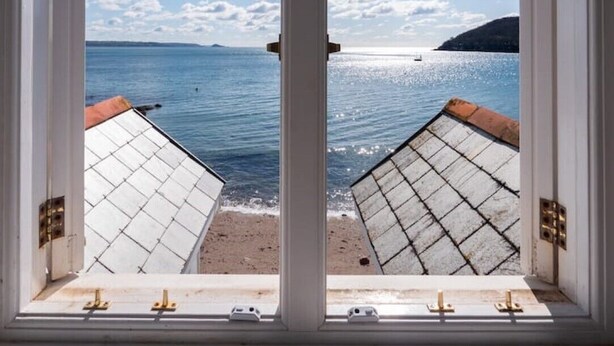 Blick durch ein Fenster auf ein Gebäude mit Blick auf einen Strand, einen klaren Himmel und ein ruhiges Meer.
