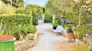 A gravel path leading to a white gate, surrounded by lush greenery and potted plants.