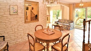 A dining area with a round wooden table, four chairs, a chandelier, and a stone wall.