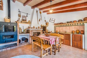 Traditional kitchen with a wood-burning stove, dining table, and kitchen utensils on display.