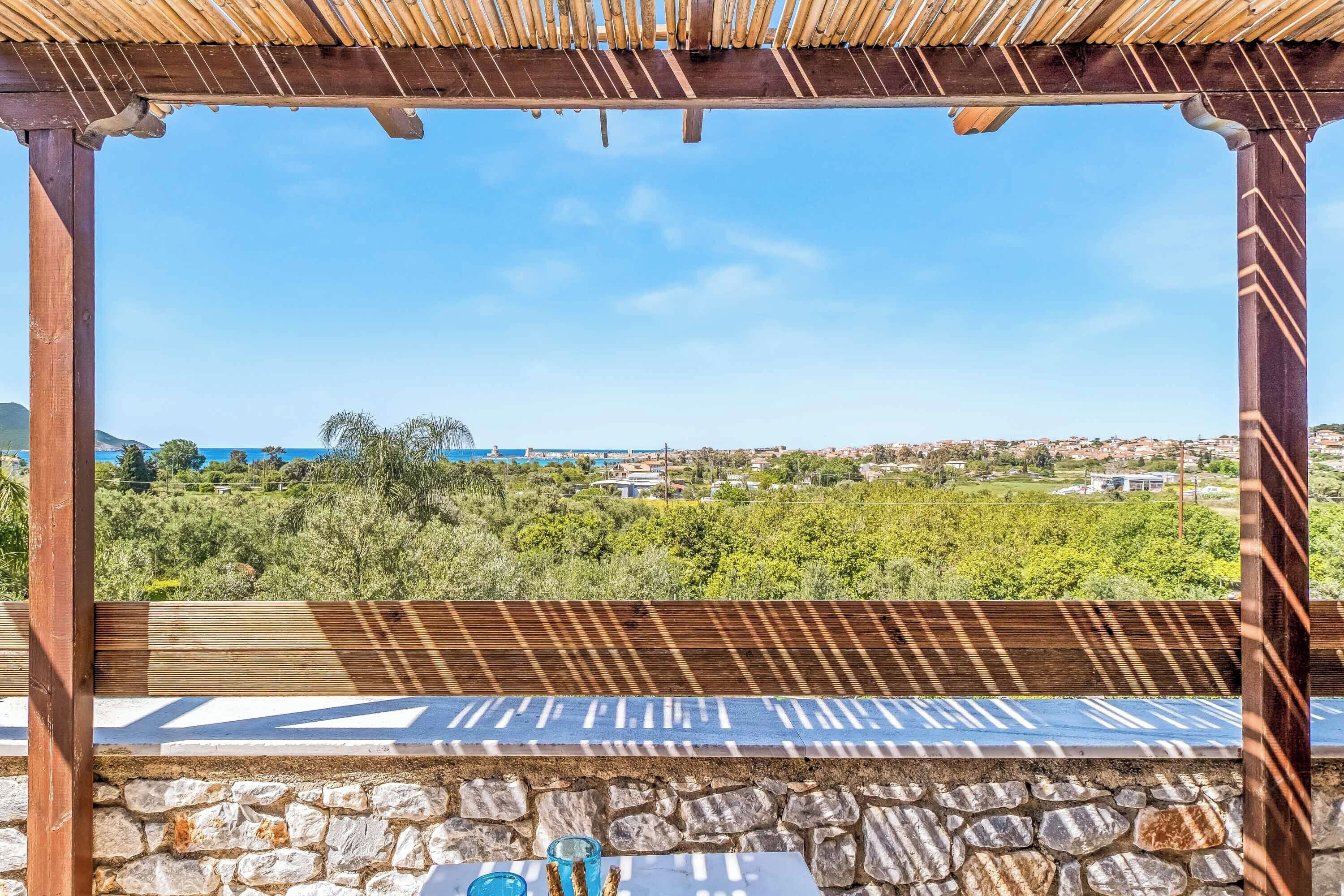 A wooden pergola with a stone wall and a view of a coastal town.
